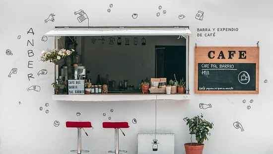 La barra de café ANBER: muro blanco con dibujos, bancos rojos y un pizarrón de Café pal barrio.